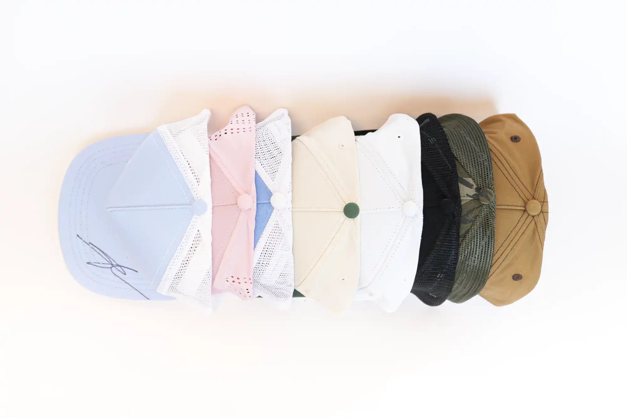 A row of seven baseball caps in various colors including light blue, pink, white, beige, black, olive green, and tan.