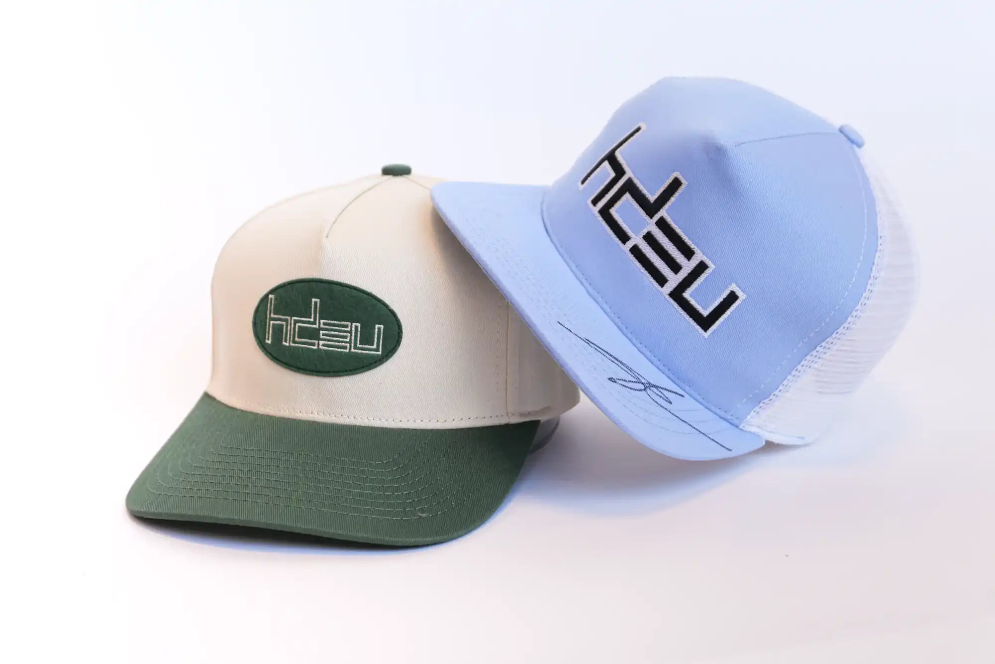 Two baseball caps, one beige and green, the other light blue and white.